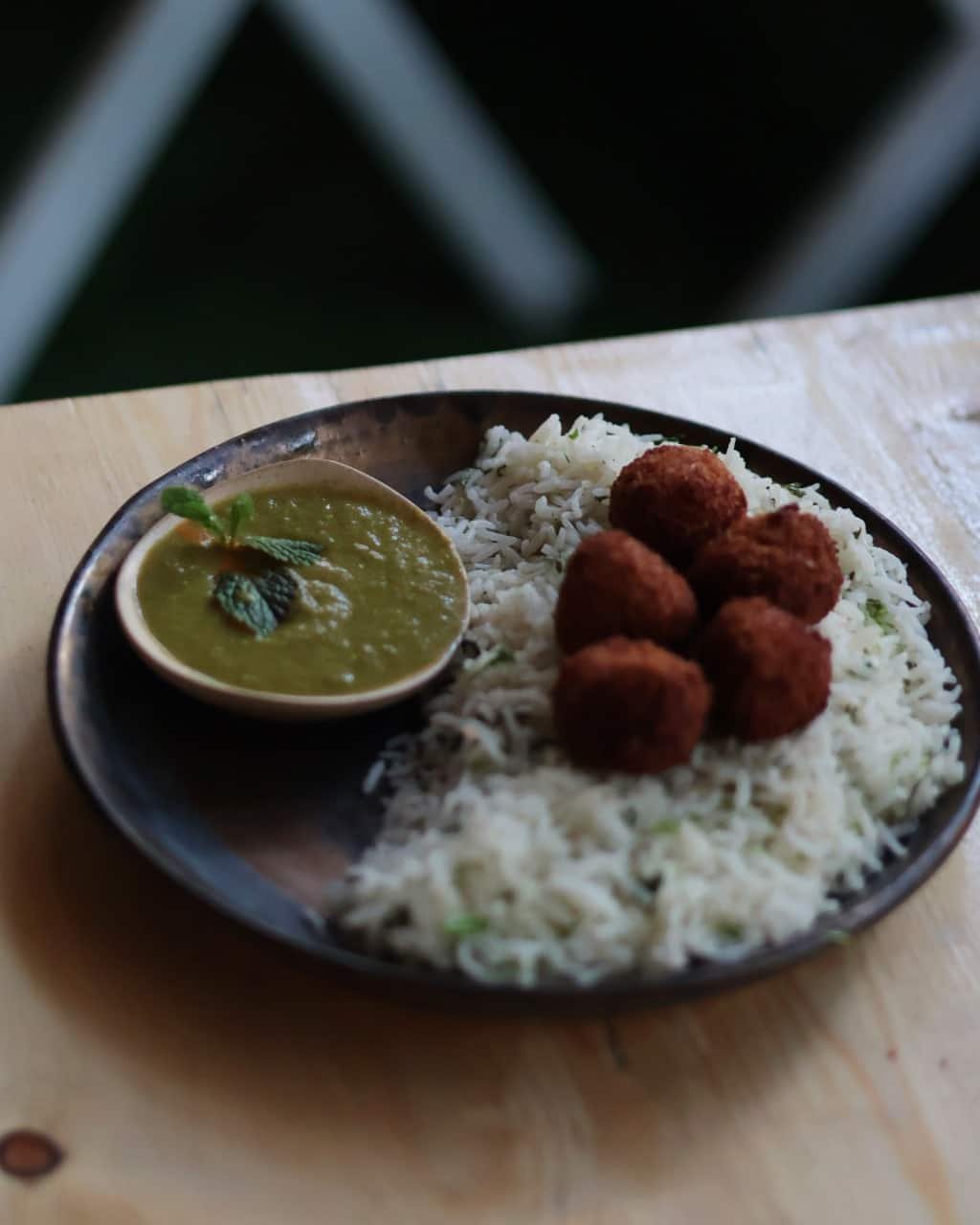 Rice with green gravy and croquettes on a dark handmade plate